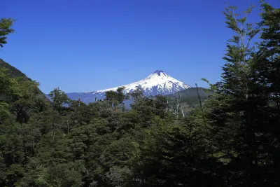 Volcán Villarrica nevado visto entre bosques desde el área del Parque Nacional Huerquehue, Araucanía, Chile.