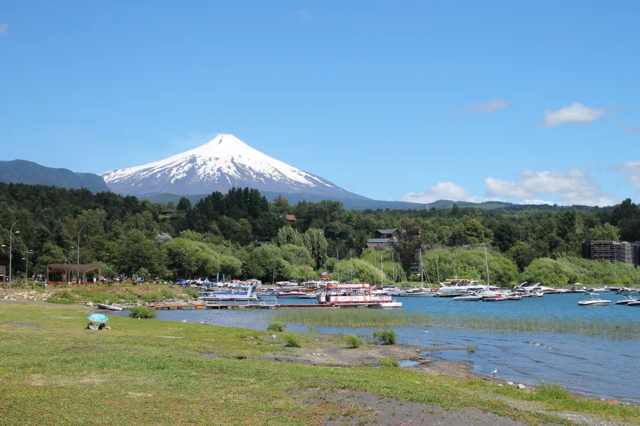 Vista panorámica del volcán Villarrica desde Pucón sobre el lago Villarrica, con embarcaciones en la orilla.